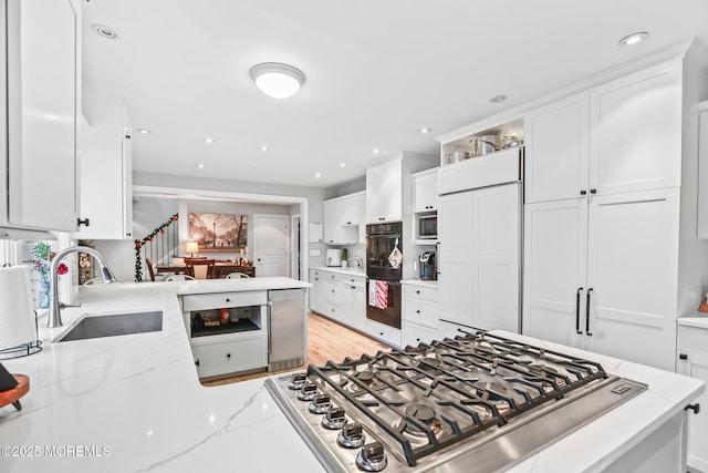 kitchen with kitchen peninsula, light stone countertops, sink, and white cabinets