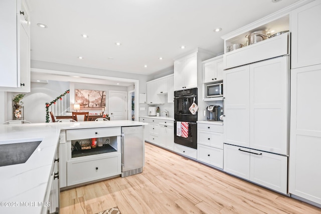 kitchen with black double oven, light hardwood / wood-style flooring, light stone countertops, built in microwave, and white cabinetry