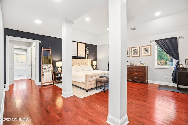 bedroom featuring wood-type flooring, connected bathroom, and decorative columns