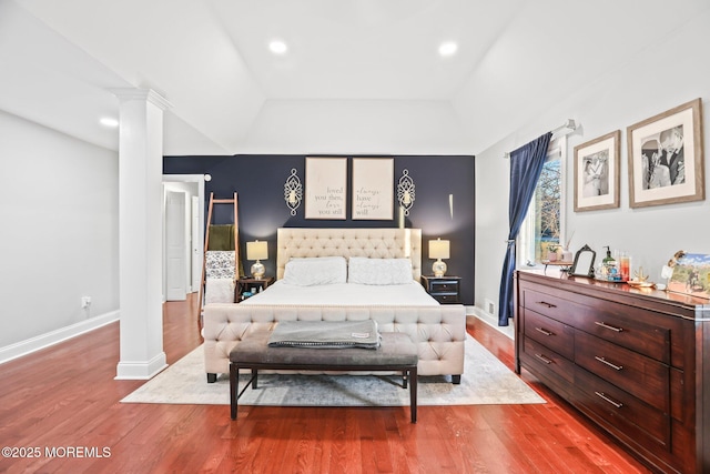 bedroom with a raised ceiling, hardwood / wood-style floors, and decorative columns