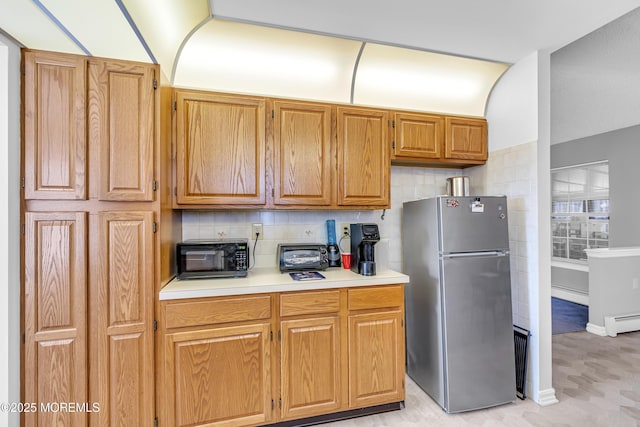 kitchen featuring backsplash, stainless steel refrigerator, and a baseboard heating unit