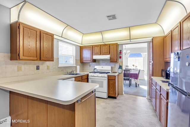 kitchen with kitchen peninsula, gas range gas stove, sink, a notable chandelier, and stainless steel refrigerator