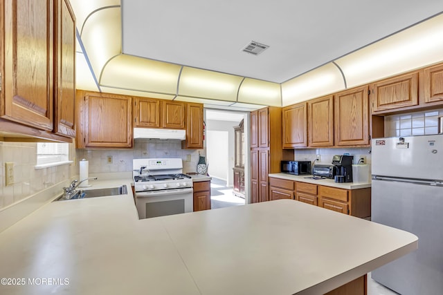 kitchen featuring sink, kitchen peninsula, white gas range oven, and stainless steel refrigerator