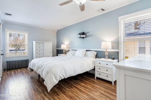 bedroom with multiple windows, radiator heating unit, ceiling fan, and wood-type flooring