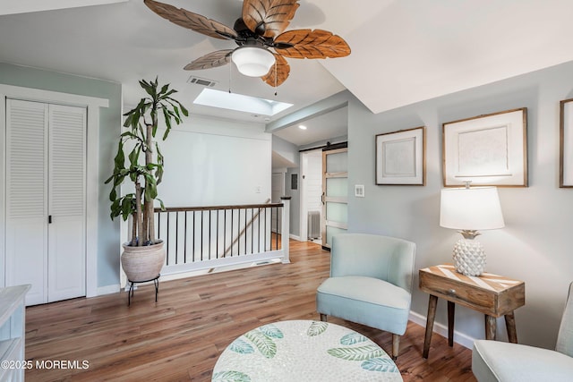 sitting room with a barn door, ceiling fan, a skylight, and hardwood / wood-style flooring