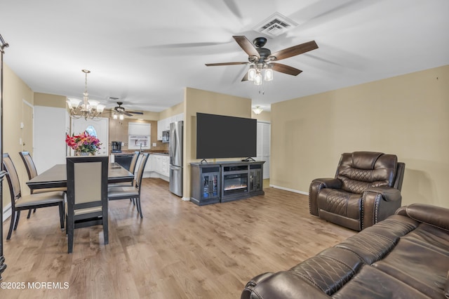 living room featuring ceiling fan with notable chandelier and light wood-type flooring