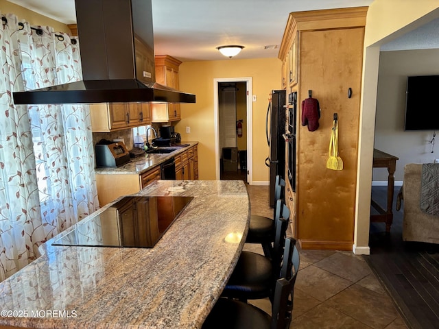 kitchen featuring island range hood, decorative backsplash, a breakfast bar area, black appliances, and baseboards
