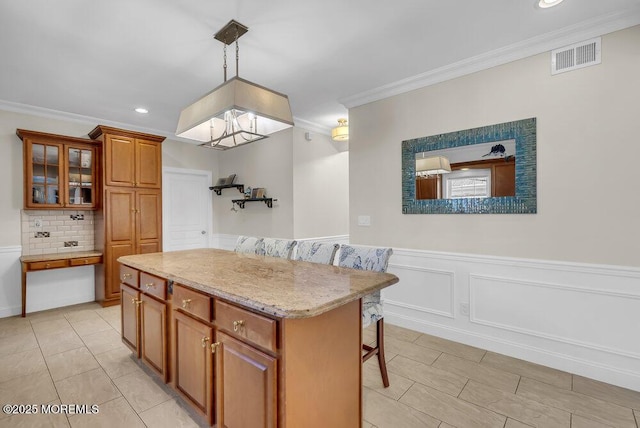 kitchen with a breakfast bar area, hanging light fixtures, a center island, light stone counters, and ornamental molding