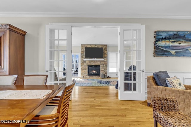 dining room with crown molding, a stone fireplace, french doors, and light wood-type flooring