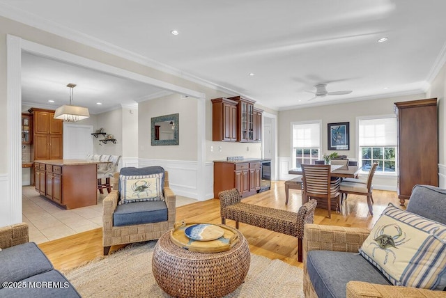 living room with ornamental molding, light hardwood / wood-style floors, ceiling fan, and indoor bar