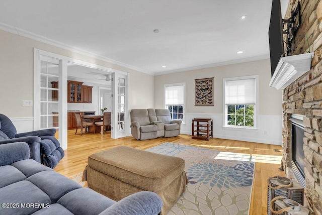 living room with ornamental molding, a stone fireplace, and light hardwood / wood-style floors