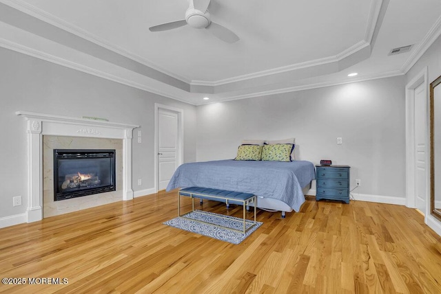 bedroom featuring crown molding, light hardwood / wood-style flooring, a tray ceiling, ceiling fan, and a fireplace