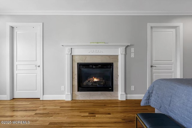 bedroom featuring a tiled fireplace, hardwood / wood-style floors, and crown molding