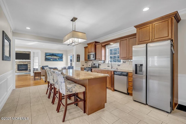 kitchen featuring sink, hanging light fixtures, stainless steel appliances, a fireplace, and light stone countertops