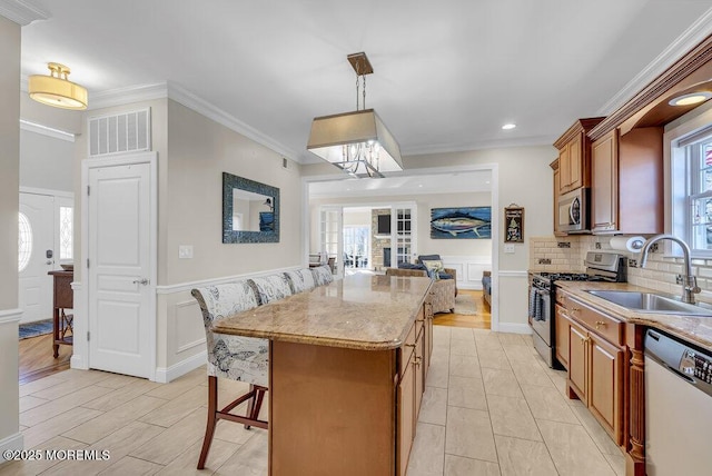 kitchen with sink, crown molding, hanging light fixtures, stainless steel appliances, and a center island