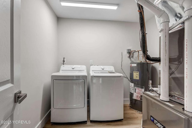 clothes washing area featuring electric water heater, light hardwood / wood-style floors, and washer and clothes dryer