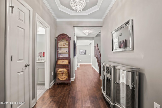 hall with a raised ceiling, ornamental molding, dark wood-type flooring, and a notable chandelier