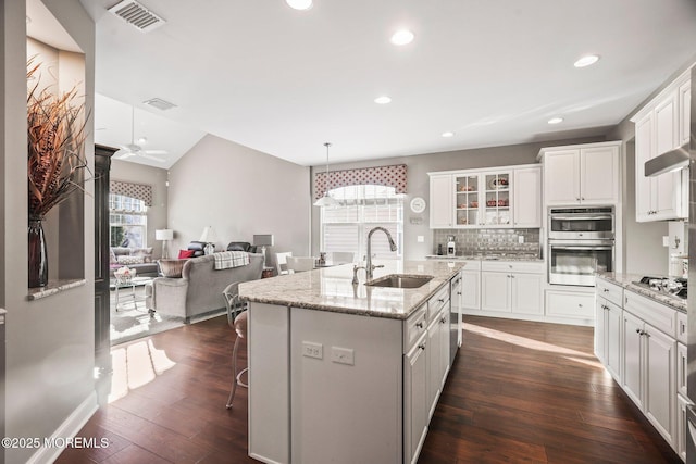 kitchen featuring a kitchen island with sink, sink, light stone countertops, and white cabinets