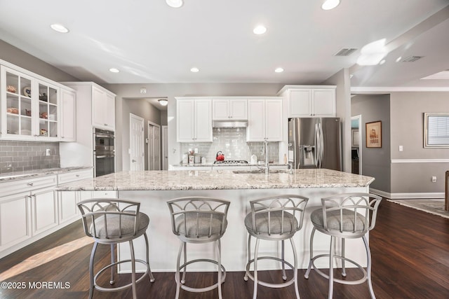 kitchen with light stone counters, stainless steel appliances, an island with sink, and white cabinets