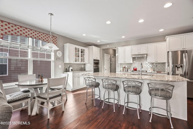 kitchen with stainless steel refrigerator with ice dispenser, a center island with sink, hanging light fixtures, and white cabinets