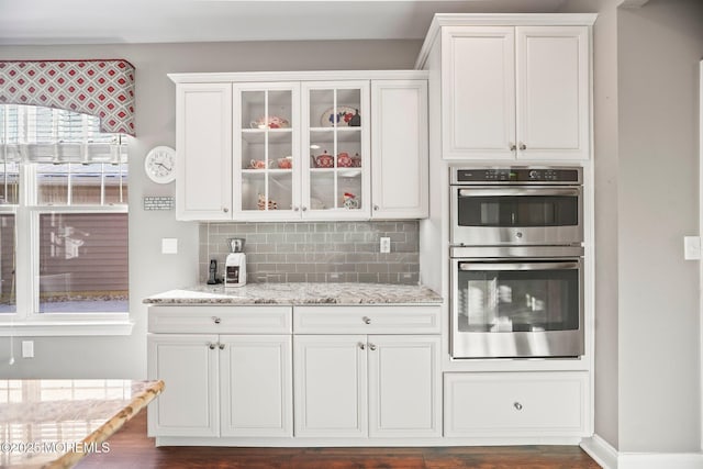 kitchen featuring white cabinets, dark hardwood / wood-style flooring, decorative backsplash, light stone countertops, and stainless steel double oven