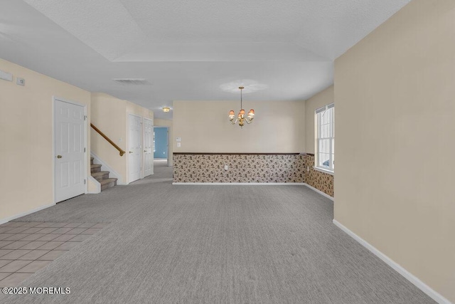 carpeted spare room with a notable chandelier and a textured ceiling