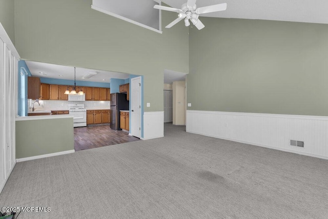 unfurnished living room featuring carpet, sink, ceiling fan with notable chandelier, and high vaulted ceiling