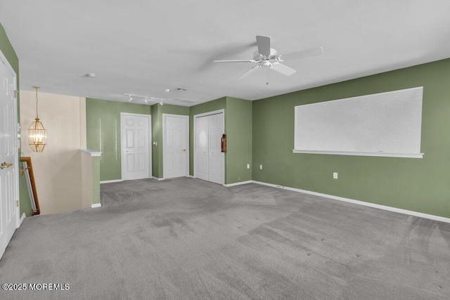 carpeted empty room with track lighting and ceiling fan with notable chandelier