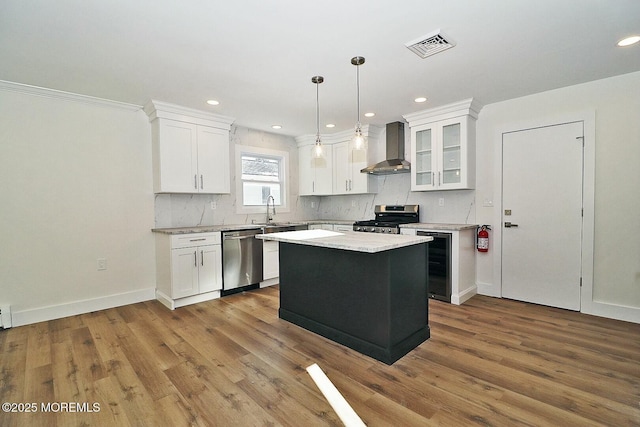 kitchen featuring white cabinets, wall chimney exhaust hood, a center island, and appliances with stainless steel finishes