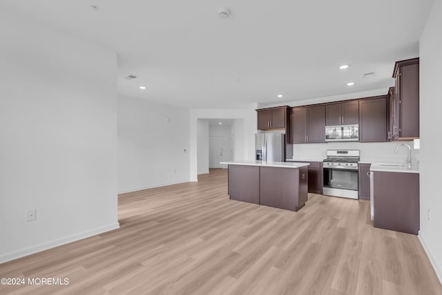 kitchen with sink, appliances with stainless steel finishes, dark brown cabinets, a kitchen island, and light wood-type flooring