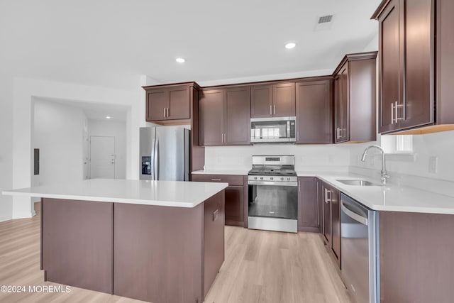 kitchen with appliances with stainless steel finishes, dark brown cabinetry, sink, light hardwood / wood-style flooring, and a center island