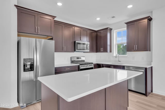 kitchen with light wood-type flooring, dark brown cabinets, stainless steel appliances, sink, and a center island