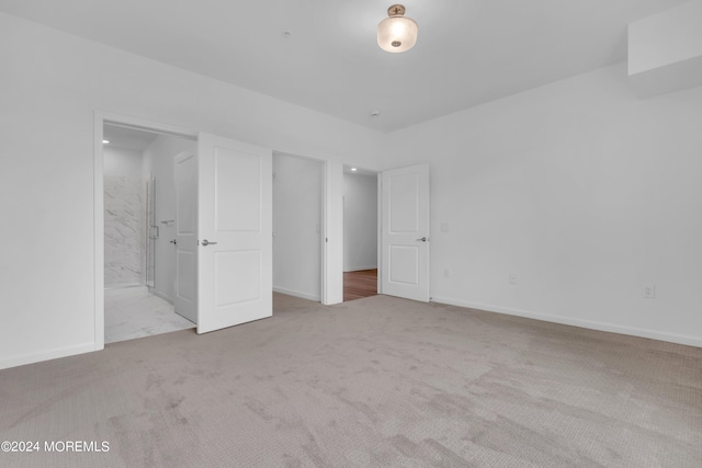 unfurnished bedroom featuring light carpet and ensuite bathroom