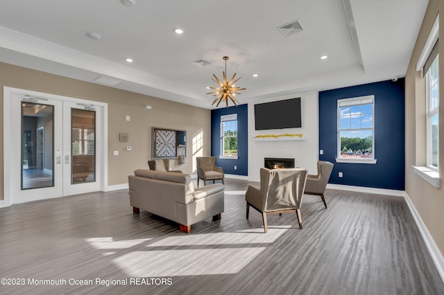 living room with french doors, a large fireplace, a tray ceiling, an inviting chandelier, and hardwood / wood-style floors