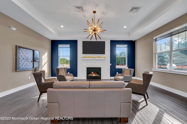 living room featuring a notable chandelier, hardwood / wood-style floors, a tray ceiling, a fireplace, and ornamental molding