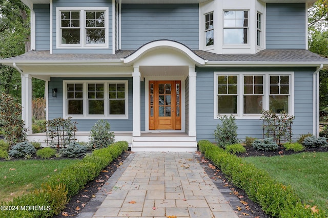 doorway to property featuring a shingled roof and covered porch