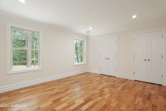 unfurnished bedroom featuring two closets, multiple windows, and crown molding