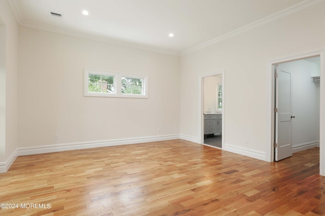 unfurnished bedroom featuring light wood-type flooring, a walk in closet, ensuite bathroom, and ornamental molding