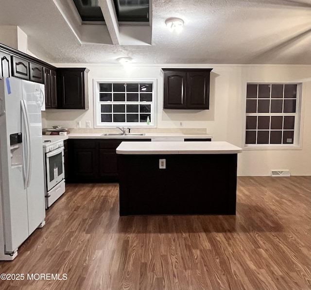 kitchen featuring sink, white appliances, dark hardwood / wood-style floors, a textured ceiling, and a kitchen island