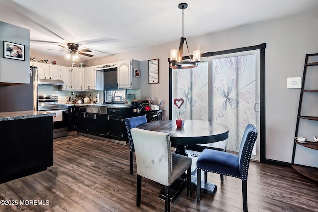 dining area with ceiling fan with notable chandelier, sink, and dark hardwood / wood-style flooring