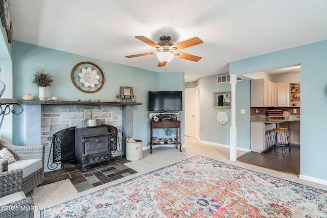 living room with a wood stove, ceiling fan, and a textured ceiling