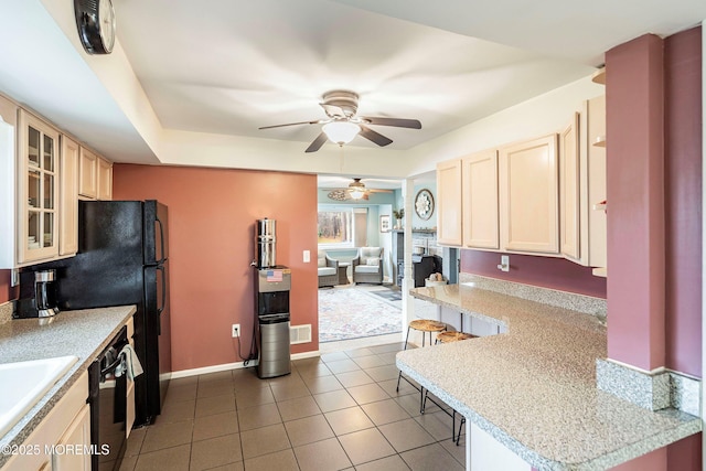 kitchen with ceiling fan, a kitchen breakfast bar, black fridge, kitchen peninsula, and dark tile patterned flooring