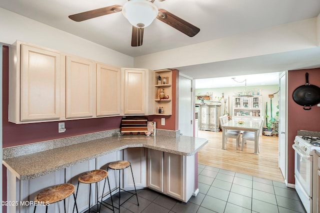 kitchen featuring kitchen peninsula, a kitchen breakfast bar, ceiling fan, white range with gas cooktop, and light tile patterned flooring