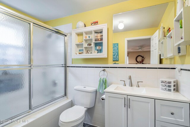 full bathroom featuring shower / bath combination with glass door, vanity, tile walls, and toilet