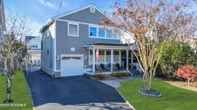 view of property featuring covered porch, a front lawn, and a garage