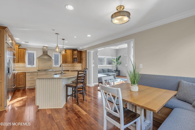 dining area featuring decorative columns, crown molding, dark hardwood / wood-style flooring, and sink