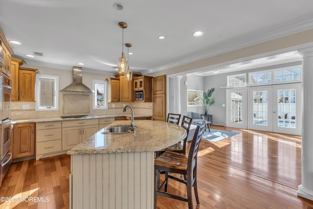 kitchen with a kitchen island with sink, a breakfast bar area, sink, wall chimney range hood, and tasteful backsplash