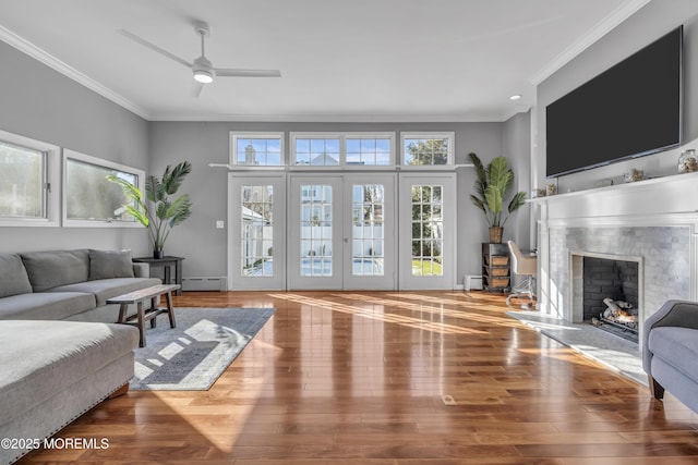 living room featuring hardwood / wood-style floors, baseboard heating, crown molding, a tiled fireplace, and ceiling fan