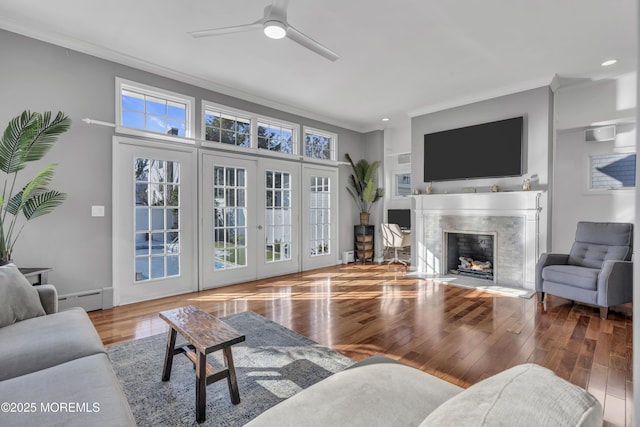 living room featuring a premium fireplace, baseboard heating, ceiling fan, and crown molding