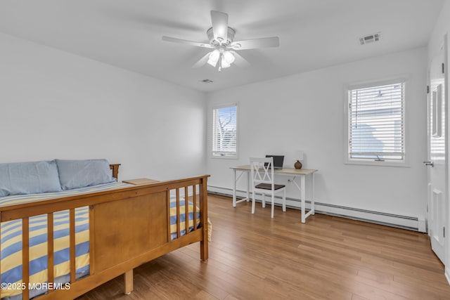 bedroom featuring a baseboard heating unit, ceiling fan, light hardwood / wood-style flooring, and multiple windows